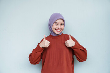 Happy young Asian Muslim woman wearing hijab with thumbs up gesture. Isolated white background.