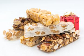 Different types of turrón (nougat), a traditional Christmas sweet in Spain, with some Christmas decoration ( a red Christmas gift), on a white background.