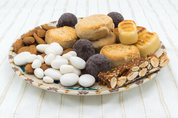 Traditional Christmas sweets in Spain: turrón, marzipan, peladillas (sugared almonds), mantecados, polvorones, chocolate balls, almonds. Set on a white tablecloth with stripes.