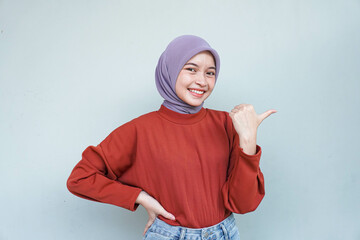 Young Asian Muslim woman smiling while pointing to copy space beside her.