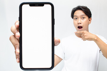 mock up of young Asian man showing and pointing at big blank screen smartphone. asian man in beige...