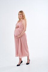 Woman in pink dress posing for photo. She is pregnant and wearing necklace. Mother love concept.