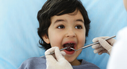 Cute arab boy sitting at dental chair with open mouth during oral checking up with doctor. Visiting...