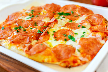 Fresh hot delicious pepperoni pizza with cheese, tomatoes and basil leaves in a pizzeria close-up.