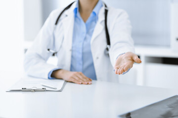Unknown woman-doctor in blue blouse is giving helping hand while sitting at the desk in clinic. Perfect medical service, medicine concept