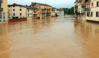 Houses on the bank of a muddy brown river during a flood are at risk of flooding after torrential...