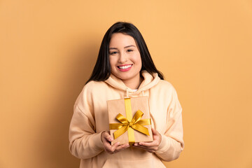 joyful brazilian woman receiving gift box in beige colors. birthday, christmas, gift box concept.