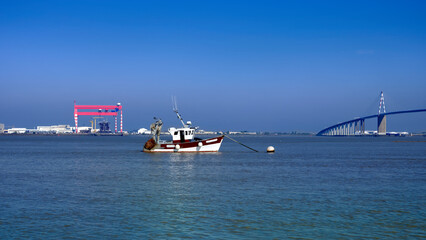 Fishing boat and the big bridge of Saint Nazaire as well as its industrial zone  at Saint Brevin les Pins in Pays de la Loire region in western France