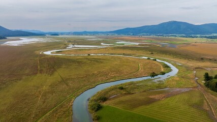 Winding river snakes through vast, green landscape dotted with Cerknica intermittent lake, Slovenia