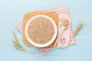 Bowl with spelt grain on wooden background, top view