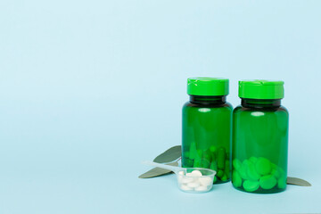 Bottles with pills and green leaves on color background