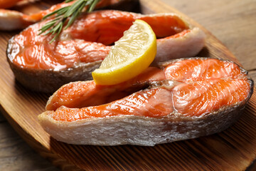 Tasty grilled salmon steaks, lemon and rosemary on wooden table, closeup