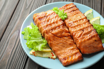 Delicious grilled salmon fillets with lettuce and lemon on wooden table, closeup