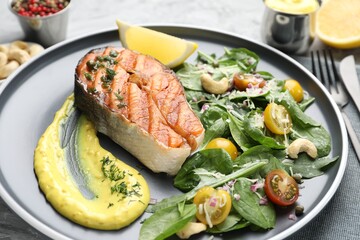 Tasty grilled salmon steak with sauce and salad on table, closeup