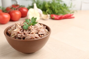 Canned meat with parsley in bowl on wooden table, closeup. Space for text
