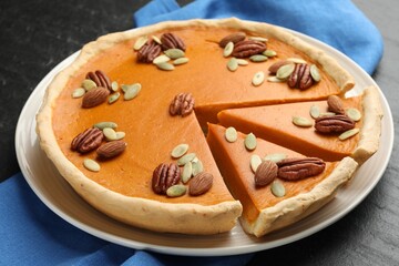 Tasty homemade pumpkin pie with seeds and nuts on black table, closeup