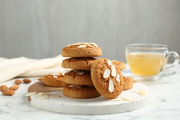 Tasty cookies with almond flakes and tea on white marble table