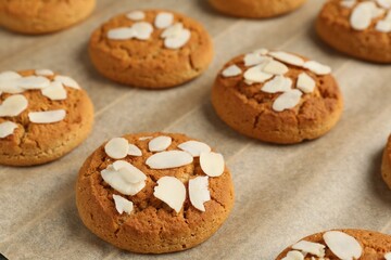 Tasty cookies with almond flakes on parchment paper, closeup