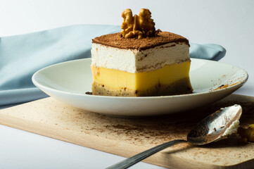 Dessert with whipped cream, custard, and walnut topping on a white plate. Tiramisu with whipped cream and walnut on a wooden board. Layered dessert with walnut, cocoa, and whipped cream garnish.