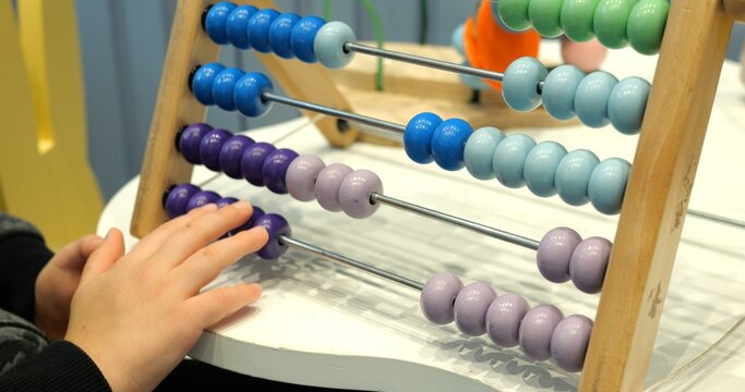 Little child solves maths tasks moving colorful beads on abacus at desk closeup. Toddler boy learns to count with old-fashioned device in preschool class