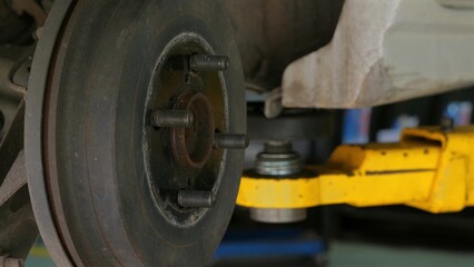 Close-up of car's brake disc and hydraulic lift in auto repair shop, illustrating maintenance and repair services in automotive industry. Auto Repair and Maintenance.