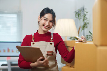 Asian sme business owner smiling and preparing a package for delivery at her home office