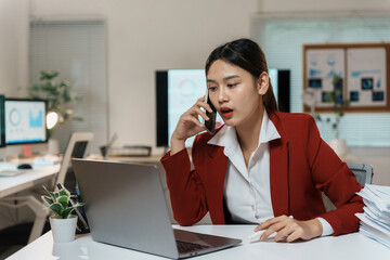 Obraz premium Businesswoman is multitasking in her office, talking on the phone while working on her laptop with a focused expression