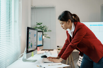 Young manager experiencing back pain while typing on a keyboard and looking at computer screen in her office