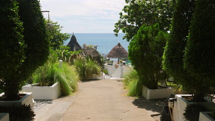 Peaceful tropical pathway leading to beachside resort with lush greenery and oceanside huts, serene...