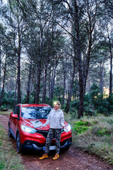 Car and adult woman lost in wooded area trying to orient herself at dusk.