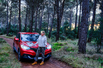 Car and adult woman lost in wooded area trying to orient herself at dusk.