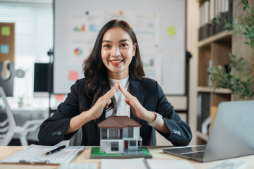 Smiling real estate agent protects a house model in her office, offering top notch service to clients in property ownership and investment