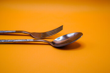 A pair of spoons and forks on an orange background.