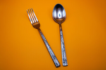 A pair of spoons and forks on an orange background.