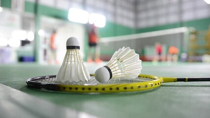 Badminton rackets and white cream badminton shuttlecocks after playing or after games on green floor in indoor badminton court soft focus concept for badminton lovers around the world.