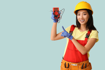 Young female electrician pointing at multimeter on blue background