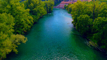 Trezzo sul Adda, Italy. Aerial view of a mountain freshwater river with low water level surrounded by green trees. White swans on the river. Forest. Hydroelectric power station. Green planet. Ecology