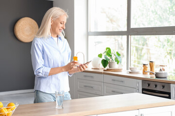 Mature woman checking pills description online in kitchen