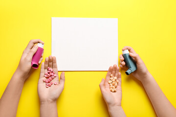 Child's hands with blank card, pills and asthma inhalers on yellow background