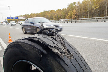 A broken tire stands on the asphalt against the background of moving cars. Warning of danger. Example of an emergency situation.