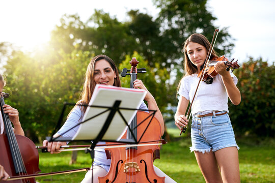 Music, learning and child with violin in park for playing, practice and lesson with teacher. Cello, nature and woman teaching kids musical instruments for talent show, performance or recital
