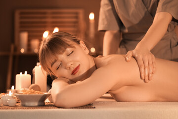Young woman undergoing massage procedure in spa salon