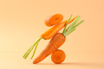 Whole and cut fresh carrots on pale orange background