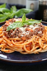 Delicious pasta bolognese with basil on black table, closeup