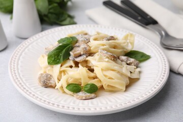 Delicious pasta with mushrooms and basil on light table, closeup