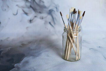 Paintbrushes in Glass Jar Against Abstract Background