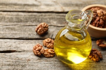 Cooking oil in jug and walnuts on wooden table, closeup. Space for text