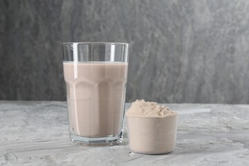 Delicious protein shake in glass and scoop with powder on grey table