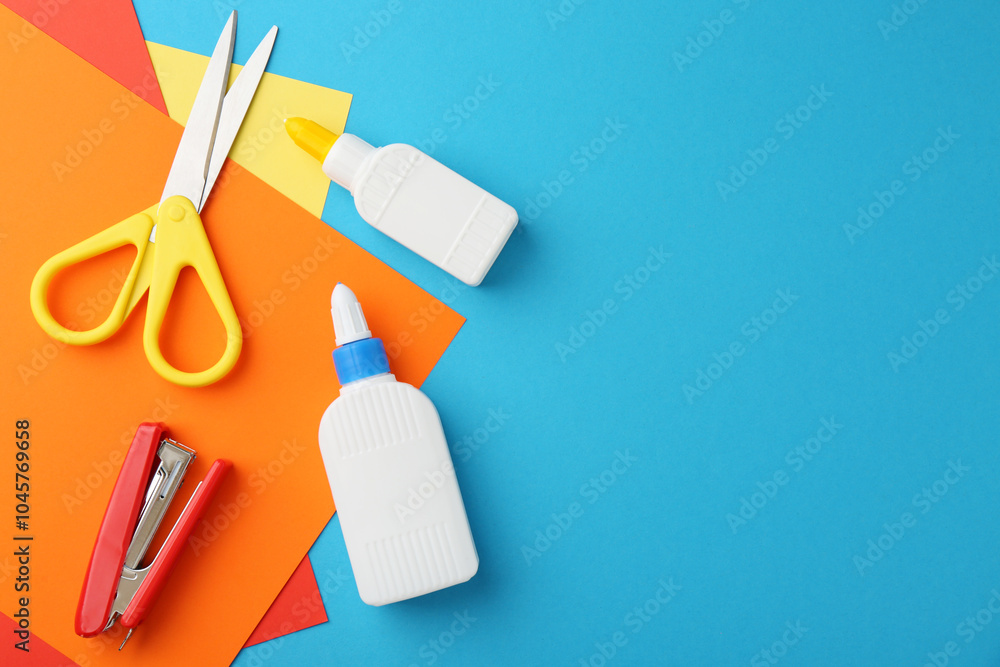 Sticker glue, colorful paper, stapler and scissors on light blue background, flat lay. space for text