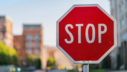 Stop road sign. Red octagon with white lettering. Blurred city bokeh on background.